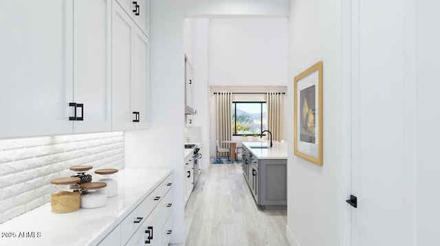 interior space with decorative backsplash, a high ceiling, light wood-type flooring, gray cabinets, and a sink