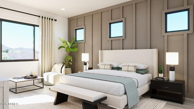 bedroom with a decorative wall, multiple windows, and light wood-style floors