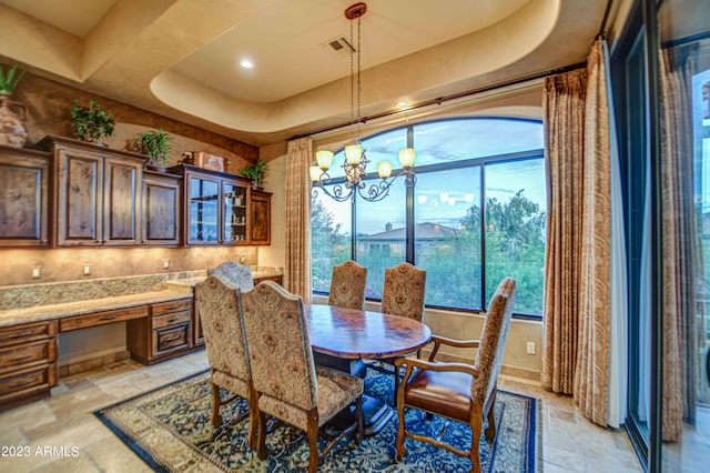 tiled dining space with an inviting chandelier, built in desk, a tray ceiling, and a healthy amount of sunlight