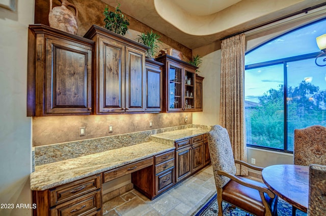 interior space featuring light stone counters, dark brown cabinetry, light tile floors, and built in desk