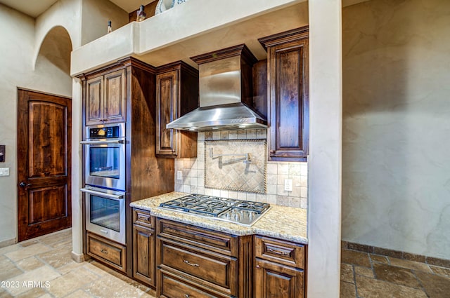 kitchen with light tile floors, light stone counters, appliances with stainless steel finishes, wall chimney range hood, and tasteful backsplash
