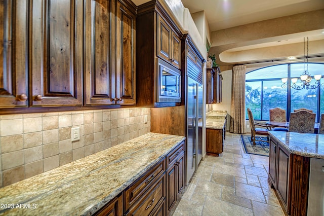kitchen featuring light stone countertops, stainless steel microwave, backsplash, a chandelier, and pendant lighting
