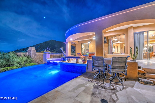 pool at night featuring a patio and a mountain view