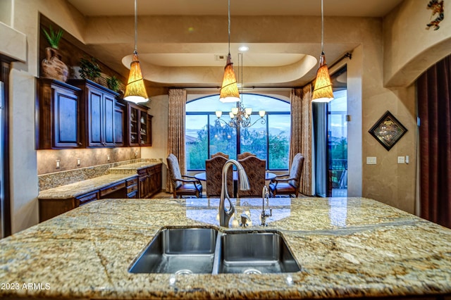 kitchen with sink, backsplash, light stone countertops, an inviting chandelier, and decorative light fixtures