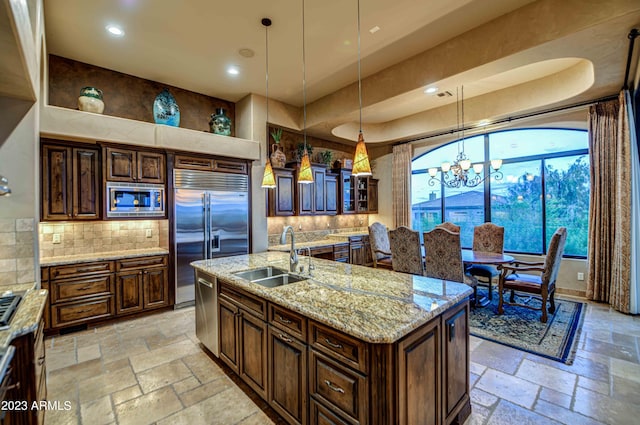 kitchen featuring hanging light fixtures, sink, a center island with sink, tasteful backsplash, and built in appliances
