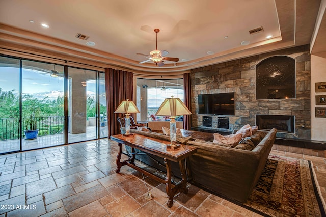 living room featuring ceiling fan, tile flooring, a raised ceiling, and a fireplace