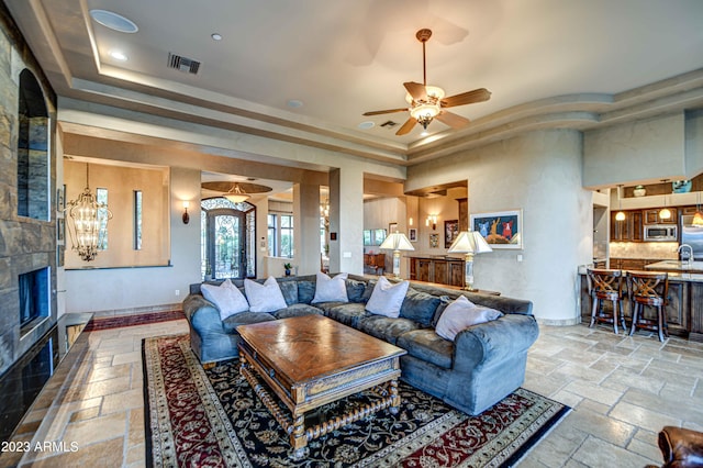 living room with a tile fireplace, light tile floors, ceiling fan, sink, and a tray ceiling