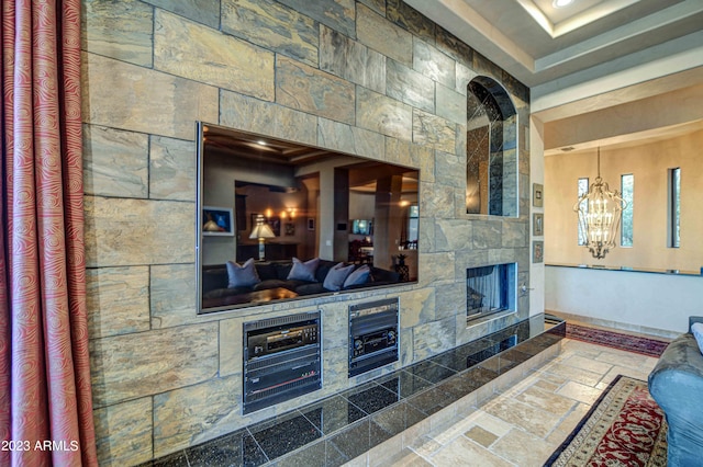 interior space featuring tile flooring, a stone fireplace, a tray ceiling, and a chandelier
