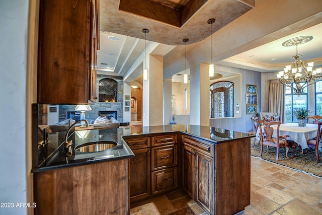kitchen with dark stone countertops, a notable chandelier, pendant lighting, a fireplace, and a raised ceiling