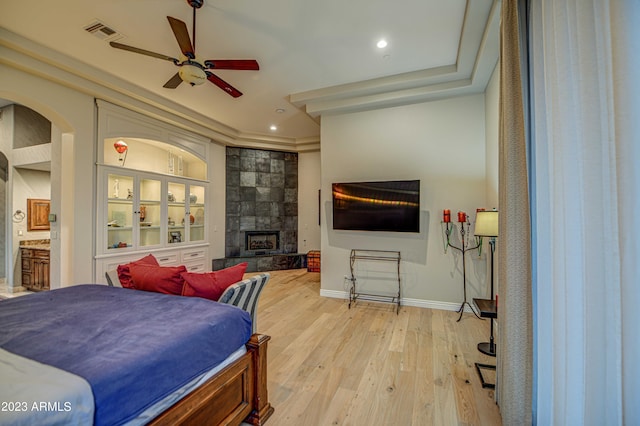 bedroom with ceiling fan, light wood-type flooring, ensuite bathroom, and a fireplace