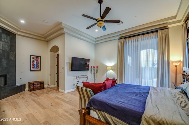 bedroom featuring a tray ceiling, ceiling fan, light hardwood / wood-style flooring, and a fireplace