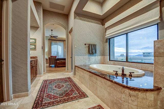 bathroom with ceiling fan, a relaxing tiled bath, tile floors, and vanity