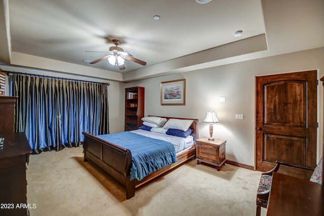 bedroom with a raised ceiling, ceiling fan, and light colored carpet
