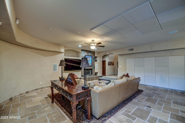 tiled living room with ceiling fan and a fireplace