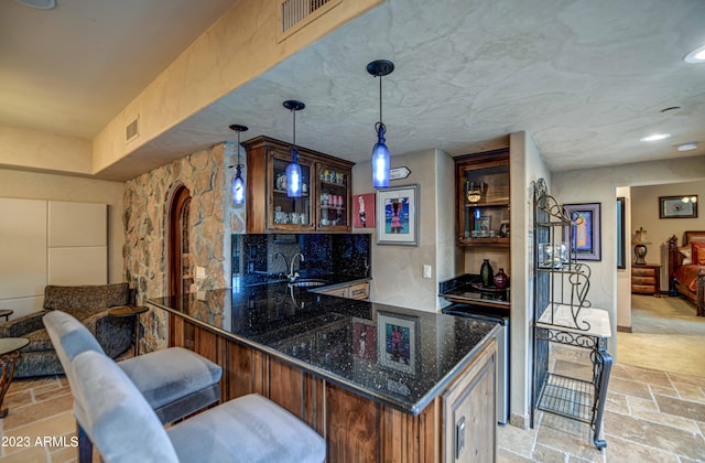bar with dark stone counters, pendant lighting, light tile floors, and sink