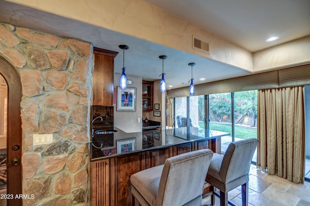 kitchen with kitchen peninsula, sink, light tile flooring, decorative light fixtures, and a kitchen bar