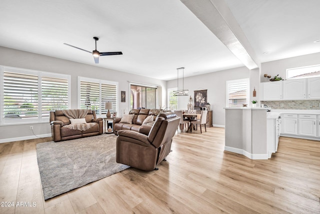 living room with beam ceiling, ceiling fan, plenty of natural light, and light wood-type flooring