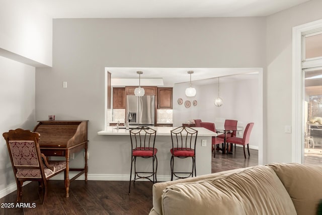 kitchen with kitchen peninsula, dark wood-type flooring, decorative light fixtures, stainless steel fridge, and a breakfast bar