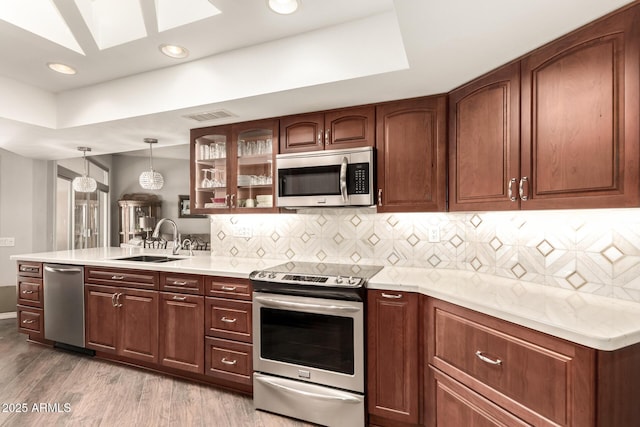 kitchen with stainless steel appliances, sink, light wood-type flooring, backsplash, and pendant lighting