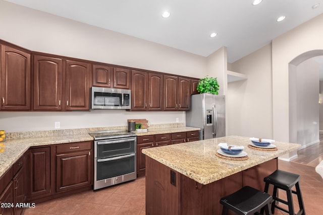 kitchen featuring stainless steel appliances, a kitchen bar, a kitchen island, light tile patterned flooring, and light stone counters