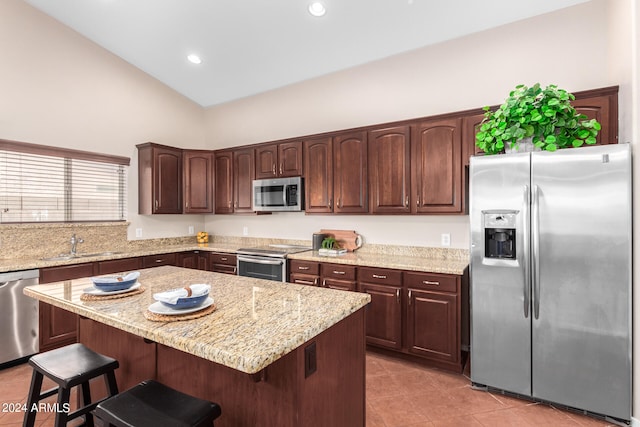 kitchen with appliances with stainless steel finishes, vaulted ceiling, a center island, and light tile patterned floors