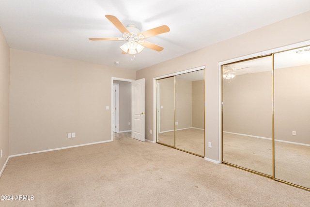 unfurnished bedroom with ceiling fan, light colored carpet, and multiple closets