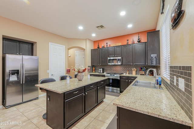 2115 N Cougar Ct, Casa Grande, AZ 85122 - kitchen featuring light tile patterned floors, a kitchen island, stainless steel appliances, arched walkways, and a sink