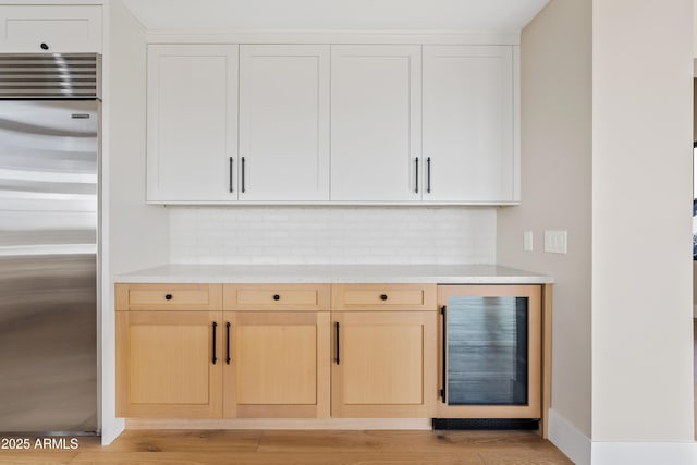 bar with backsplash, light brown cabinets, white cabinetry, stainless steel built in fridge, and wine cooler