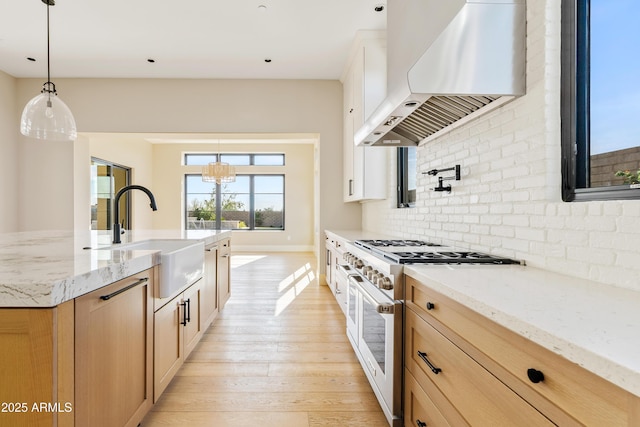 kitchen with sink, stainless steel stove, decorative light fixtures, and wall chimney range hood