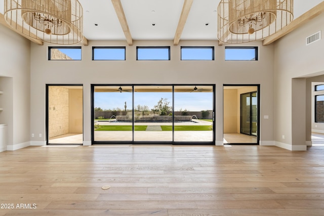 unfurnished living room featuring built in features, a towering ceiling, and light wood-type flooring