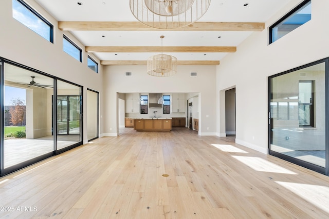 unfurnished living room with plenty of natural light, beamed ceiling, light hardwood / wood-style floors, and ceiling fan with notable chandelier