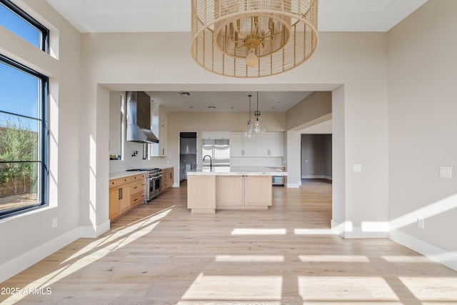 kitchen featuring decorative backsplash, wall chimney exhaust hood, a kitchen island with sink, pendant lighting, and double oven range