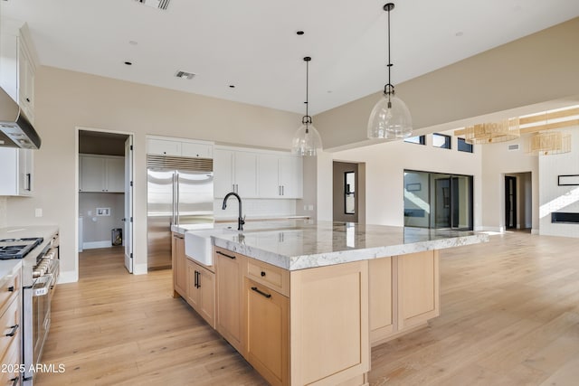 kitchen with white cabinets, light stone counters, a large island, and sink