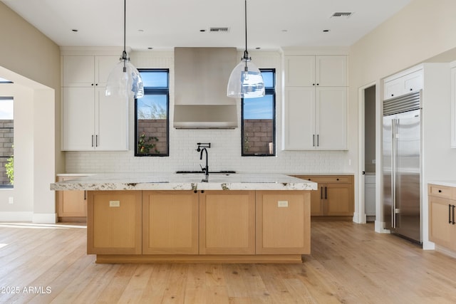 kitchen with a kitchen island with sink, white cabinets, ventilation hood, built in refrigerator, and decorative light fixtures