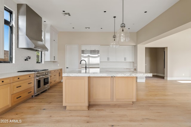 kitchen featuring wall chimney exhaust hood, a kitchen island with sink, white cabinets, and high end appliances