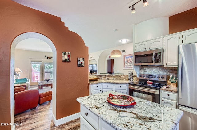 kitchen featuring light wood-style flooring, stainless steel appliances, arched walkways, white cabinetry, and backsplash