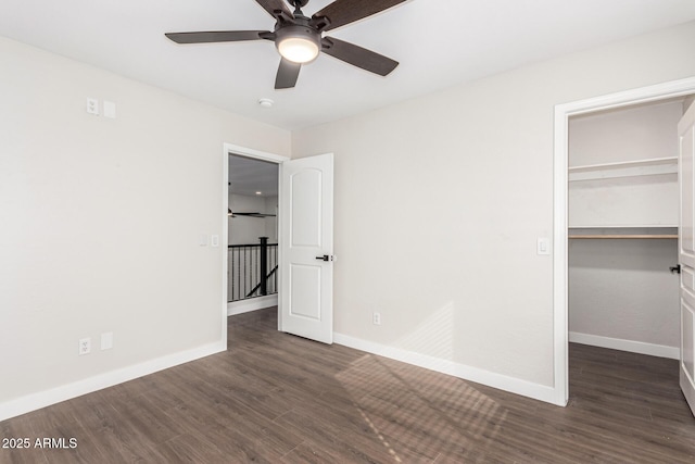 unfurnished bedroom with a spacious closet, dark wood-type flooring, a closet, and ceiling fan