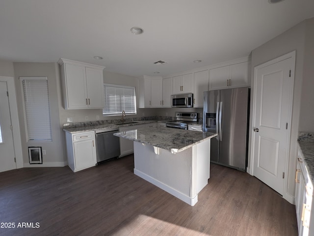 kitchen with light stone counters, white cabinetry, a center island, appliances with stainless steel finishes, and dark hardwood / wood-style floors