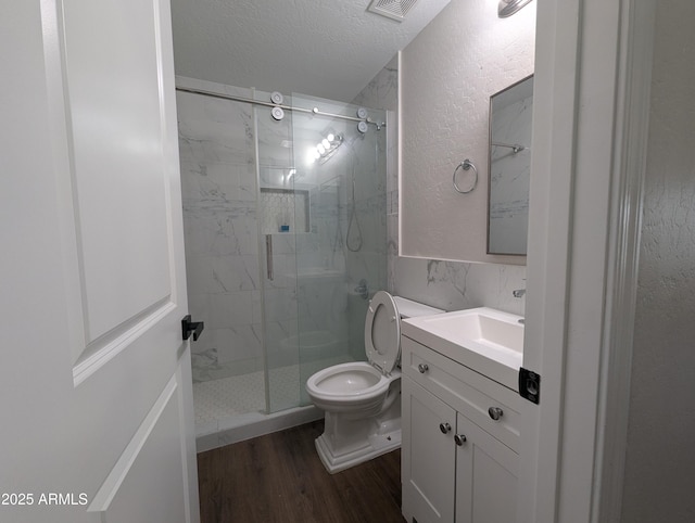 bathroom with hardwood / wood-style floors, vanity, toilet, a shower with door, and a textured ceiling