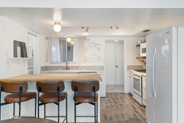 kitchen featuring white cabinetry, sink, light hardwood / wood-style floors, white appliances, and a kitchen bar