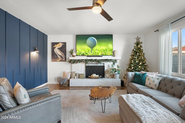 living room featuring ceiling fan, wood-type flooring, and a brick fireplace