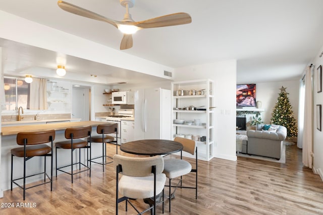 dining space featuring a fireplace, ceiling fan, sink, and light wood-type flooring