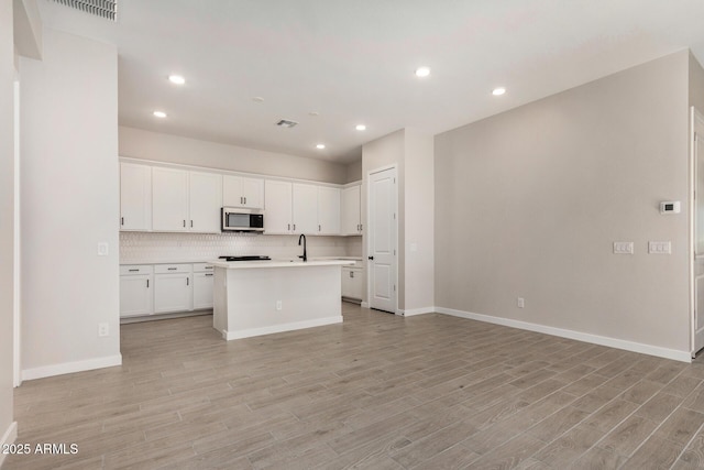 5664 N 205th Ln, Buckeye, AZ 85396 - kitchen featuring stainless steel microwave, light wood-type flooring, light countertops, open floor plan, and white cabinetry