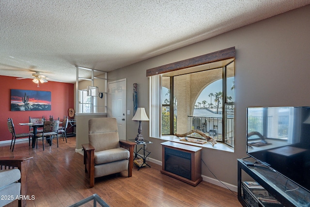 living area with ceiling fan, wood-type flooring, and a textured ceiling