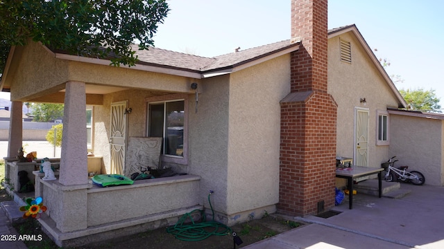 view of side of home with a patio, a chimney, roof with shingles, and stucco siding