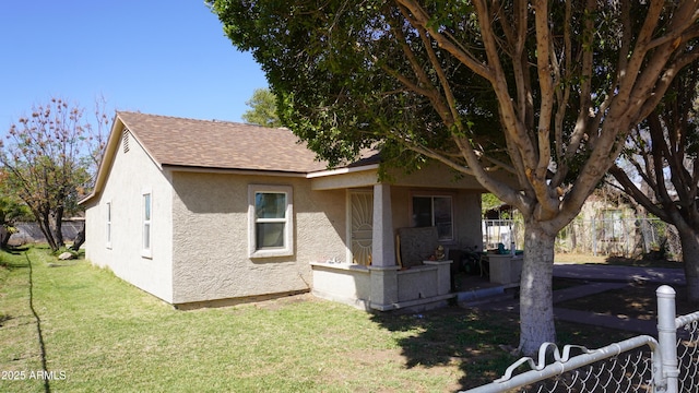 view of home's exterior featuring stucco siding, a lawn, roof with shingles, and fence