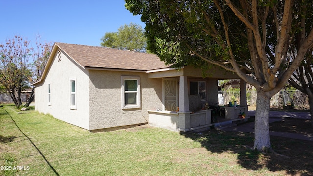 exterior space with stucco siding, a shingled roof, a yard, and fence