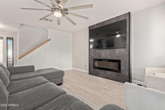 living area with light wood-style floors, ceiling fan, a fireplace, and stairs