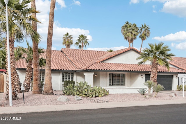 mediterranean / spanish-style house with a garage, a tiled roof, driveway, and stucco siding