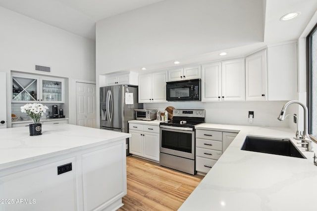 kitchen with light stone counters, a sink, visible vents, white cabinets, and appliances with stainless steel finishes